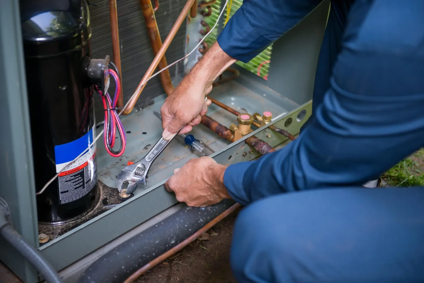 Close-up of a service model repairing copper fittings inside an open air-conditioning condenser